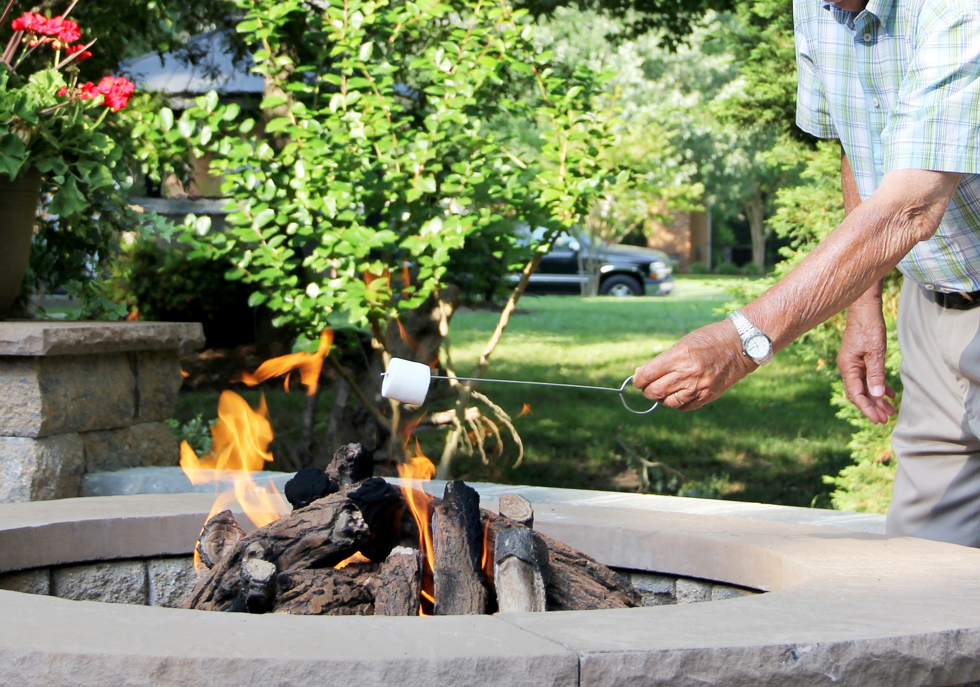 Elderly man in the backyard enjoying the fire pit & marshmallows during an outdoor gathering.