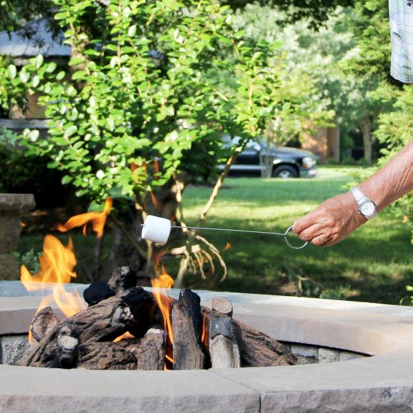 Elderly man in the backyard enjoying the fire pit & marshmallows during an outdoor gathering.